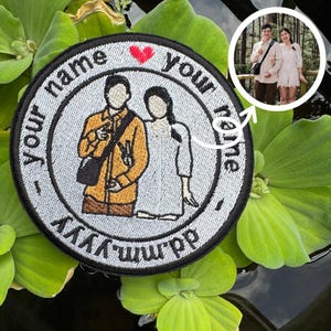 Op de afbeelding: Geborduurde ronde patch met een paar illustratie, de tekst "your name" en een hart. De patch heeft een zwarte rand en een lichtgrijze achtergrond. Een kleine foto van het paar staat in de rechterbovenhoek. De datum is ook opgenomen.