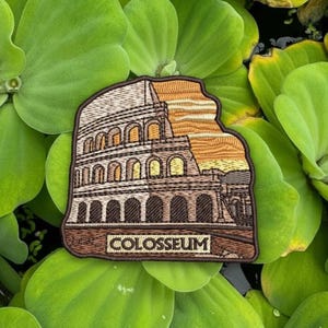 May include: Embroidered patch featuring the Colosseum in Rome, Italy, with a sunset backdrop. The patch is brown and beige with the word "COLOSSEUM" at the bottom. The patch is surrounded by green aquatic plants.