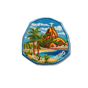 May include: A shield-shaped embroidered patch featuring a landscape of Rio de Janeiro with the Christ the Redeemer statue atop a mountain, palm trees, a beach, and blue sky. The text RIO DE JANEIRO is stitched in white at the bottom edge.