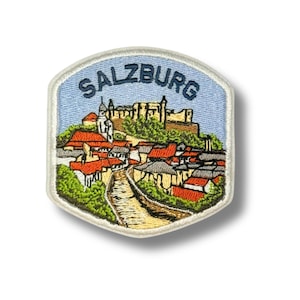 May include: Embroidered patch featuring a detailed illustration of Salzburg, Austria. The design includes a cityscape with red-tiled roofs, a fortress, and the word "SALZBURG" in blue lettering against a light blue sky background. The patch has a cream-colored border.