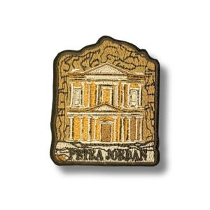 May include: Embroidered patch depicting a building facade with columns and a triangular pediment. The patch is in shades of brown and gold, with the text "PETRA JORDAN" at the bottom. The patch has an irregular shape, resembling a piece of rock.