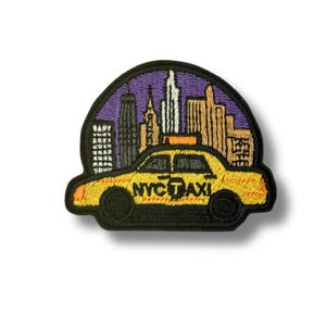 Pode incluir: Patch bordado com um táxi amarelo de Nova York com o texto "NYC TAXI" em preto. O táxi está situado em um céu roxo e um horizonte com edifícios em laranja, branco e preto. Borda preta.