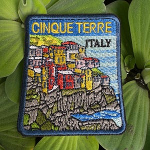 May include: Embroidered patch featuring a colorful illustration of the Cinque Terre region of Italy. The patch has a blue background with the text "Cinque Terre" and "Italy" in white.