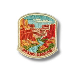 May include: Embroidered patch featuring a scenic view of the Grand Canyon. The patch showcases the canyon's red rock formations, a blue river, and a blue sky. The words "GRAND CANYON" are embroidered in red along the bottom edge.