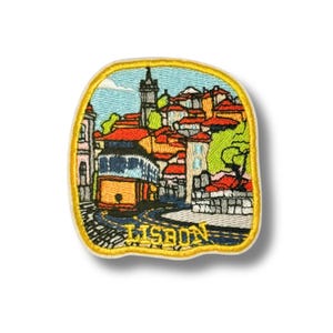 May include: Embroidered patch featuring a colorful depiction of Lisbon, Portugal. The design includes a yellow tram, red-tiled roofs, and the word "LISBON" in yellow. The patch has a yellow border and is set against a white background.