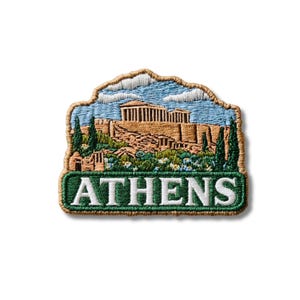 May include: An embroidered patch featuring a landscape of the Parthenon in Athens, Greece. The design includes tan stone ruins, green trees, a blue sky with white clouds, and a dark green banner at the bottom with the white text ATHENS.