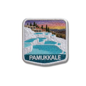May include: A square embroidered patch with rounded corners featuring a landscape of the Pamukkale thermal pools in Turkey. The design shows white travertine terraces filled with bright blue water, buildings, and a sunset sky. The word PAMUKKALE is stitched in white capital letters at the bottom.