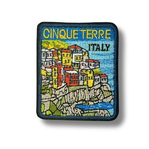 Op de afbeelding: Geborduurde patch met de dorpen Cinque Terre in Italië. De patch heeft een blauwe rand en de tekst "CINQUE TERRE ITALY" in geel en blauw. De afbeelding toont kleurrijke gebouwen op een klif met een blauwe zee.