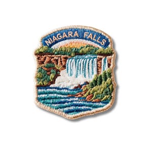 May include: An embroidered patch featuring a landscape of Niagara Falls with a blue sky, white cascading water, brown rocky cliffs, and green foliage. The text NIAGARA FALLS is stitched in light blue letters along the top curved border.