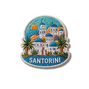 Puede incluir: Un parche bordado que muestra una vista de Santorini con edificios blancos, cúpulas azules y palmeras sobre un cielo turquesa con un sol naranja. La palabra SANTORINI está bordada en letras mayúsculas blancas en la parte inferior.