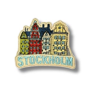 Peut inclure: Écusson brodé représentant une rangée de bâtiments colorés, dont une tour rouge et un bâtiment jaune. Le mot "STOCKHOLM" est brodé en bleu clair sur une bannière incurvée en dessous.