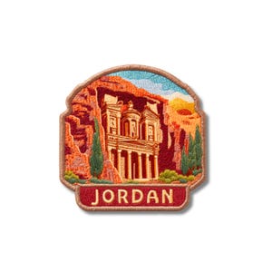 May include: An embroidered patch featuring a detailed depiction of the Treasury at Petra carved into red sandstone cliffs. The design includes green cypress trees, a blue sky, and a red banner at the bottom with the word JORDAN in cream letters.