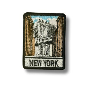 Może przedstawiać: Haftowana naszywka przedstawiająca most na Manhattanie w Nowym Jorku w czerni i bieli, otoczona budynkami. Tekst "NEW YORK" jest wyświetlany białymi literami na dole naszywki.