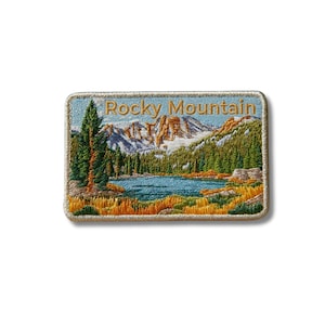 Peut inclure: Un écusson rectangulaire brodé représentant un paysage avec un lac bleu, des pins verts et des montagnes enneigées. Le texte Rocky Mountain est cousu en fil doré sur le haut de l'écusson, qui possède une bordure beige clair.