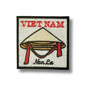 May include: Embroidered patch featuring a Vietnamese conical hat, or Non La, with the word "VIET NAM" in red above it. The hat is beige with a brown and gold band, and red ribbons hang down. The patch has a black border.