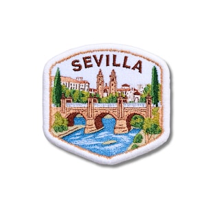 May include: A shield-shaped embroidered patch featuring a colorful scene of a bridge over a blue river with buildings and trees in the background. The word SEVILLA is stitched in brown thread at the top against a white background with a white border.