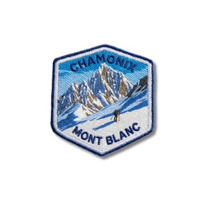 Peut inclure: Un écusson brodé hexagonal représentant un paysage de montagne enneigé du Mont Blanc. Le motif inclut un petit skieur, un ciel bleu, et le texte "CHAMONIX" en haut et "MONT BLANC" en bas en lettres brodées bleu foncé.