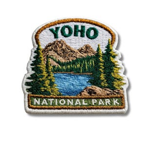 Könnte beinhalten: Ein gestickter Aufnäher mit einer Landschaft des Yoho-Nationalparks. Das Design zeigt einen blauen See, grüne Kiefern und braune Berge unter dem Schriftzug YOHO oben und NATIONAL PARK auf einem grünen Banner unten mit weißer Schrift.