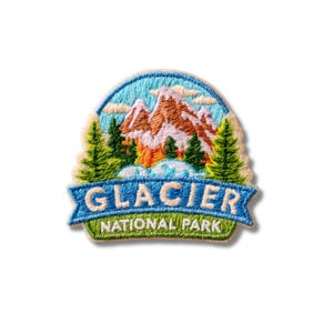 Puede incluir: Un parche bordado que muestra un paisaje de montaña con picos marrones, pinos verdes y un cielo azul claro. Una banda azul en la parte inferior muestra el texto blanco GLACIER NATIONAL PARK sobre un primer plano de hierba verde.