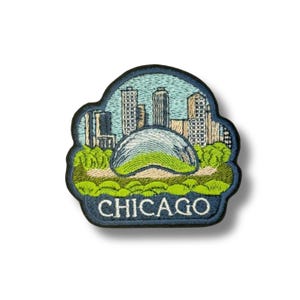 Puede incluir: Parche bordado con el horizonte de Chicago, incluyendo la escultura Cloud Gate. El parche tiene un borde azul y la palabra "CHICAGO" en blanco. El diseño utiliza tonos verdes, azules y beige.