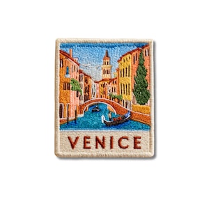 Puede incluir: Un parche bordado rectangular que presenta una escena colorida de Venecia, Italia. El diseño muestra un canal con una góndola, un puente de piedra y edificios multicolores bajo un cielo azul. La palabra VENICE está bordada en rojo abajo.