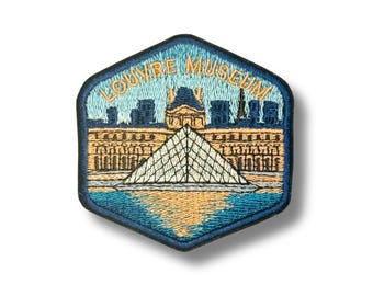 Può includere: Una toppa ricamata esagonale che raffigura il Museo del Louvre con la sua iconica piramide di vetro. Il design utilizza fili nei toni del blu, beige e oro, con il testo LOUVRE MUSEUM arcuato in oro su uno sfondo di cielo azzurro.