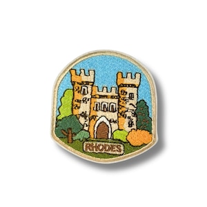 Puede incluir: Parche bordado con un castillo de dos torres, una puerta arqueada marrón y la palabra "RHODES" en un óvalo verde. El castillo es de color beige con un fondo de cielo azul y follaje verde y naranja.