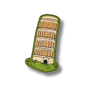 May include: An embroidered patch depicting the Leaning Tower of Pisa. The tower is rendered in shades of beige and tan with dark outlines, featuring multiple levels of arched columns. It is set against a green base with a thick green border.