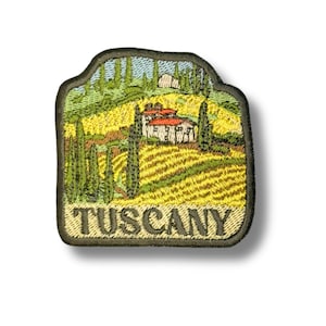 Può includere: Toppa ricamata raffigurante un paesaggio toscano con dolci colline, cipressi e un edificio con tetto di tegole rosse. La parola "TUSCANY" è ricamata in verde scuro in basso.