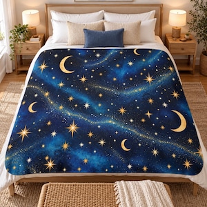 May include: A plush blanket featuring a deep blue celestial pattern with golden crescent moons and various sizes of sparkling stars scattered across a swirling nebula-like background, draped over a bed with white pillows and a blue accent pillow.
