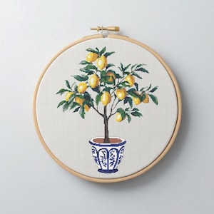 May include: A cross-stitch pattern of a lemon tree in a blue and white patterned pot. The tree has green leaves and yellow lemons.