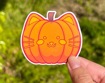 May include: A die-cut sticker featuring a cartoon cat-pumpkin hybrid. The sticker has an orange body with a brown stem and a white outline. The cat-pumpkin has cat ears, whiskers, and a smiling face. The sticker is held against a green, blurred background.