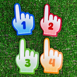 May include: Four foam finger-shaped cutouts arranged in a grid. Each cutout features a pointing index finger and a bold number in the centre. The top left is blue with the number 1, top right is red with 2, bottom left is green with 3, and bottom right is orange with 4.