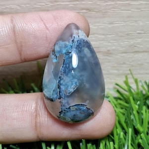 以下が含まれることがあります： 半透明の淡いグレーのベースを持つ、涙の形をした宝石。石には、独特のパターンを作り出す、印象的な青とターコイズのインクルージョンがあります。研磨された表面は光を反射し、石の自然な美しさを際立たせています。