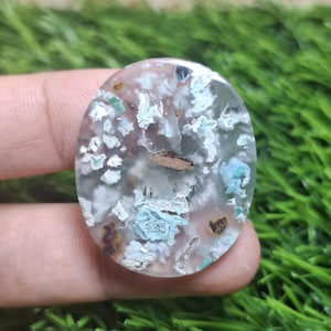 Puede incluir: Una gema ovalada con una base translúcida, que muestra patrones blancos, azules y marrones. La superficie pulida revela intrincadas formaciones internas. La apariencia general es natural y orgánica, con un diseño texturizado único.