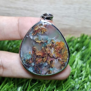 May include: A teardrop-shaped pendant with a silver-colored metal frame. The pendant features a colorful stone with a mix of brown, orange, green, and blue hues. The stone has a unique, natural pattern. The pendant is designed for wear as a necklace.