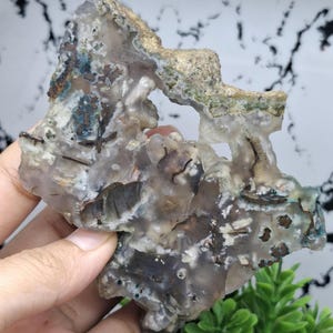 May include: A large, irregularly shaped piece of agate with a translucent, white, and grey base. The agate has brown, green, and blue inclusions and a rough, natural texture.
