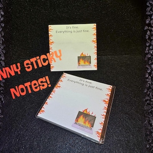 May include: Two white sticky note pads with the text "It's fine. Everything is just fine." and a graphic of a fireplace with flames. The pads have orange flame borders. The words "FUNNY STICKY NOTES!" are in orange.