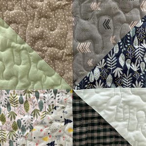 May include: Close-up of a patchwork quilt with various fabric patterns. The quilt features triangles of green, gray, and white fabrics with different textures and designs, including polka dots, arrows, and floral prints. The quilt is machine quilted.