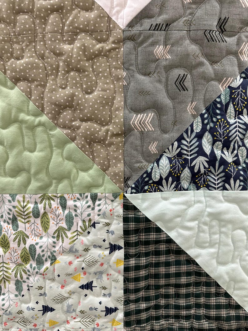 May include: Close-up of a patchwork quilt with various fabric patterns. The quilt features triangles of green, gray, and white fabrics with different textures and designs, including polka dots, arrows, and floral prints. The quilt is machine quilted.