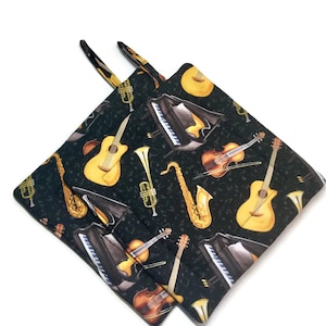 May include: A pair of black pot holders with a musical instrument pattern. The pattern includes a guitar, violin, trumpet, saxophone, and piano keys. The background is black with musical notes.