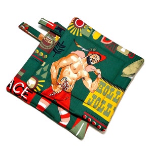 Peut inclure: Deux maniques vertes avec un motif de Noël festif. Une manique représente un homme avec une canne en sucre rayée rouge et blanche et le texte "EGG NOGG". L'autre manique représente le texte "PEACE".