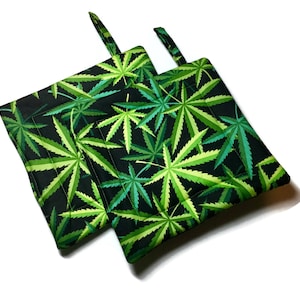 May include: Two black pot holders with a green marijuana leaf pattern. The pot holders have a loop handle.