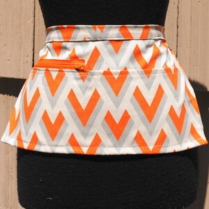 May include: A white and orange chevron patterned apron with a zippered pocket.