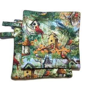 May include: Two green, brown, and blue pot holders with a birdhouse and bird pattern. The pot holders have a loop handle.