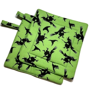 May include: Three lime green square pot holders with black witch silhouettes and witch hats. Each pot holder has a loop for hanging. The pot holders are stacked on top of each other.