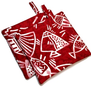 May include: Two red pot holders with a white fish pattern. The pot holders have a loop handle.