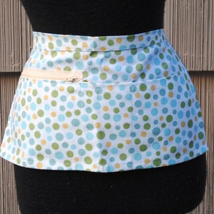 May include: A white apron with a blue and yellow polka dot pattern. The apron has a zippered pocket on the front.