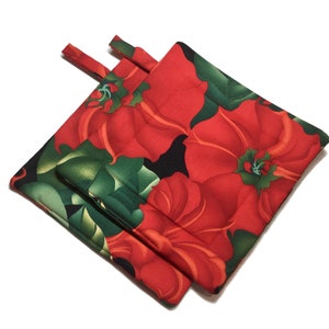 May include: Two red and green floral pot holders with a black background. The pot holders are made of fabric and have a quilted texture.