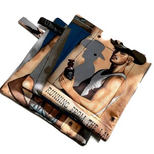 May include: A brown and tan fabric pouch featuring a cowboy holding a bottle with a skull and crossbones. The pouch has the text "RUNNING FROM THE LAW" printed on it.